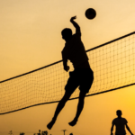 People playing beach volleyball at sunset